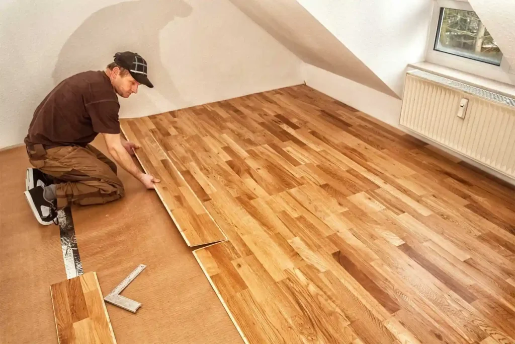 Professional installing hardwood flooring planks in attic room